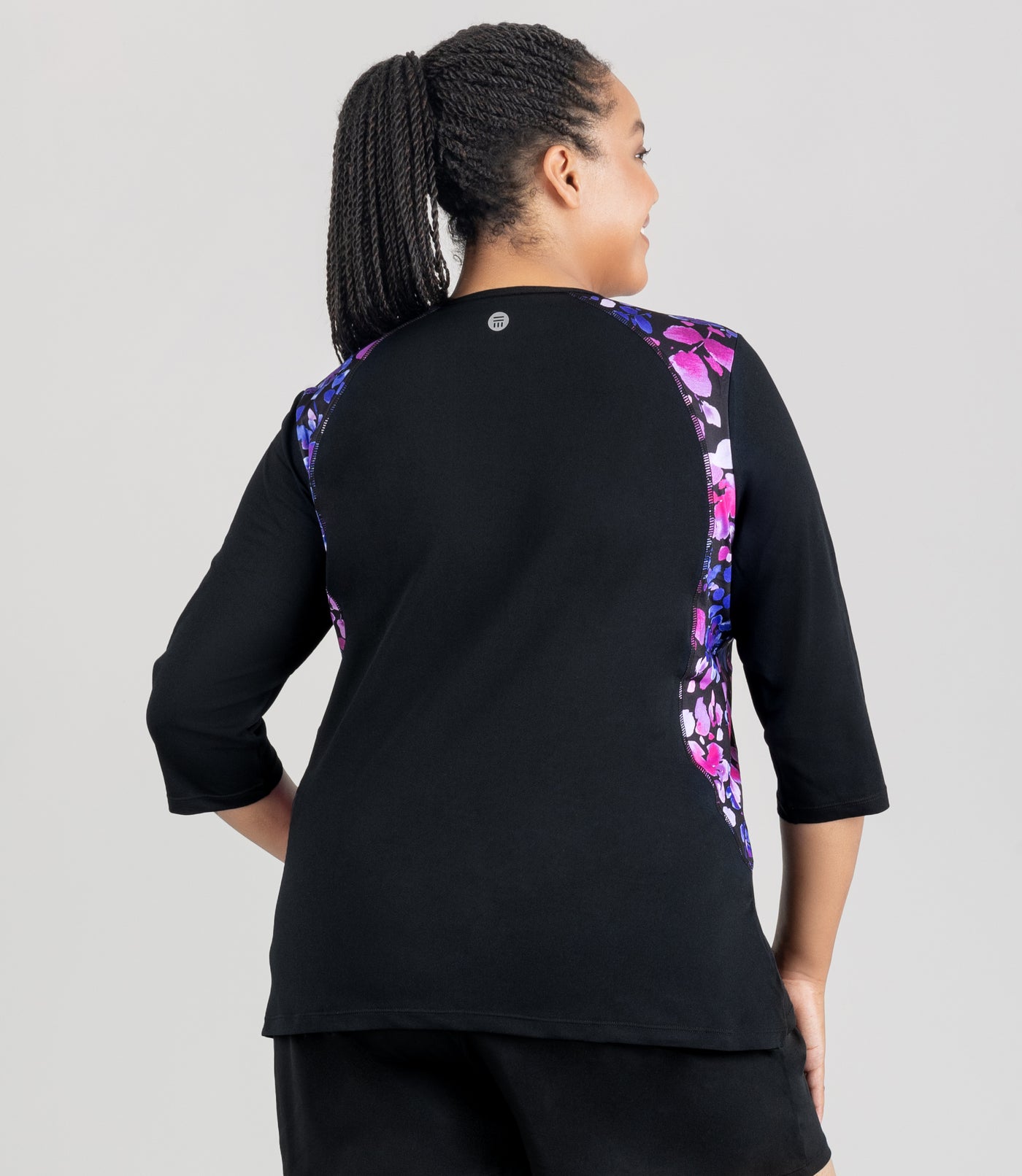 JunoActive model, facing back, wearing Aquasport three quarter sleeve rash guard in blue and pink floral elegance print. Hands are by her side.