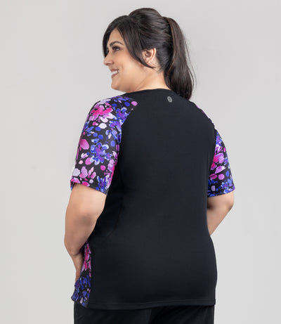 Model is facing back, wearing JunoActive's Aquasport Color Block Swim Tee with pink and blue floral elegance print on majority of front and sleeves. Back torso is in black.