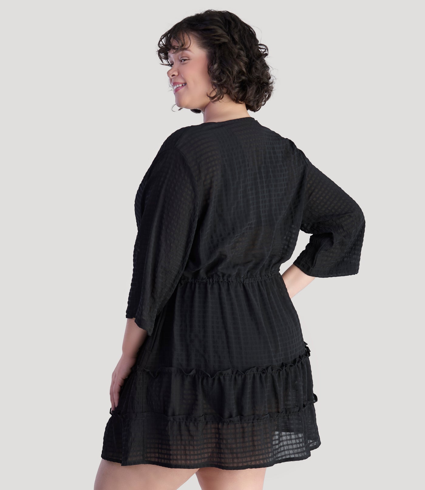 Plus size model, facing back, wearing JunoActive's BellaStyle Tie Front Tiered Cover-Up in color black.