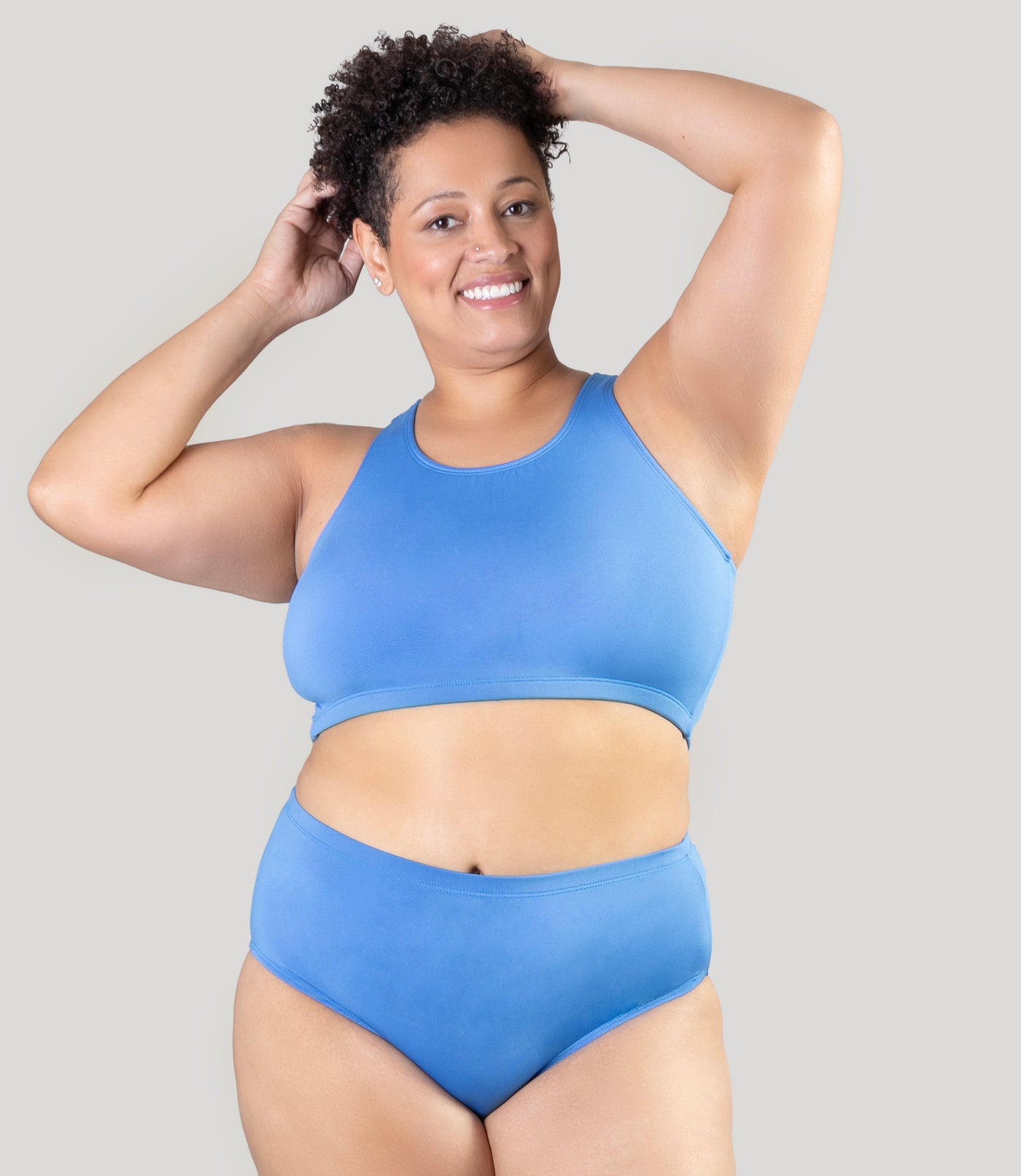 Plus size woman, facing front, wearing JunoActive QuikWik plus size Racerback Bra in Columbia Blue. The woman is wearing coordinating plus size underwear in the same color.