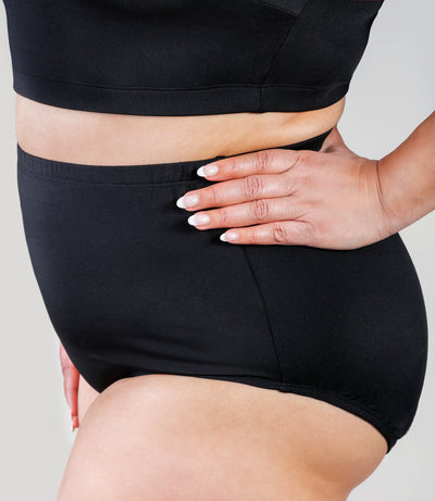 Close up of plus size person, facing side, wearing JunoActive's QuikWik Full Fit plus size Brief in color black on a gray background.