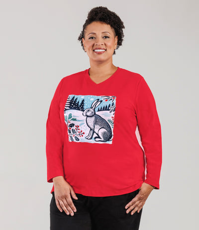 Plus size woman, facing forward, with her arms by her side, wearing JunoActive Designer Graphic Stretch Naturals plus size Long Sleeve V-Neck Top in red featuring a graphic of a Winter Hare. She is wearing JunoActive Plus Size Leggings in the color Black.