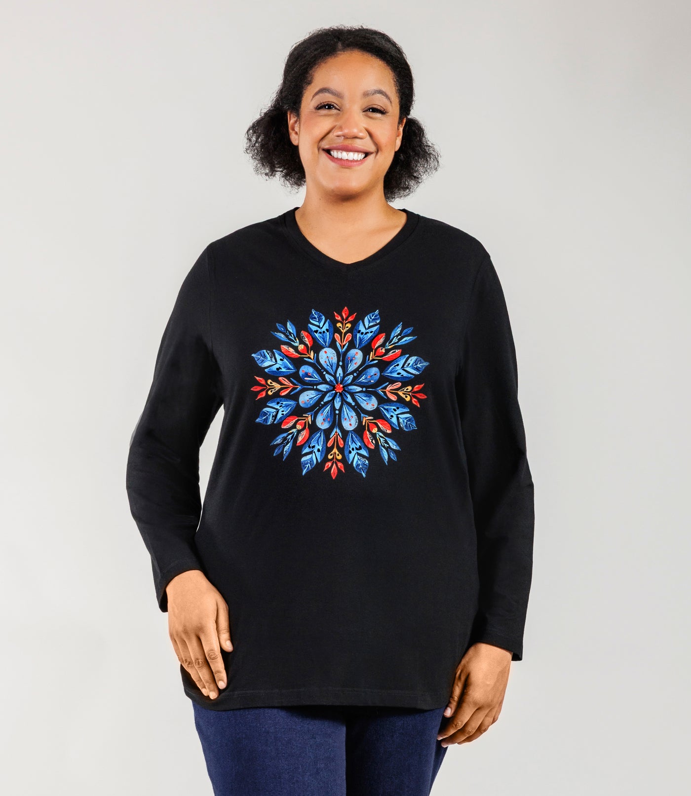Plus size Woman, facing front, wearing a JunoActive black plus size long sleeve shirt with colorful scandi inspired snowflake design.