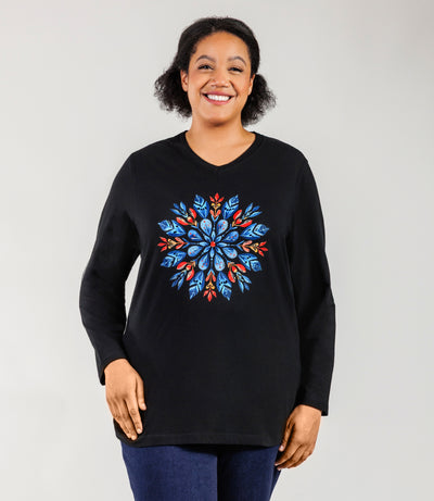 Plus size Woman, facing front, wearing a JunoActive black plus size long sleeve shirt with colorful scandi inspired snowflake design.