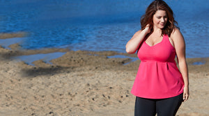 Plus size woman on beach in JunoActive pink plus size tankini swim top and black JunoActive swim shorts