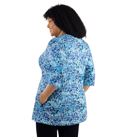 JunoActive Lifestyle Cotton three quarter sleeve pocketed tunic in print Monet. Model facing back with one hand in shirt.