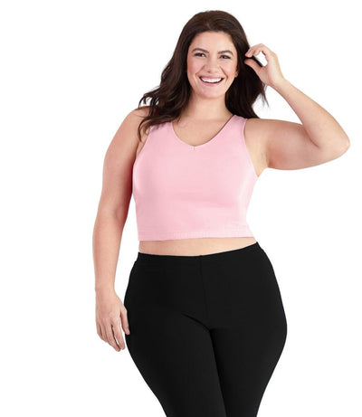 Plus size woman, facing front, wearing JunoActive plus size SupraKnit Long-Line V-Neck Bra top in Petal Pink. The woman is wearing black JunoActive plus size leggings. 