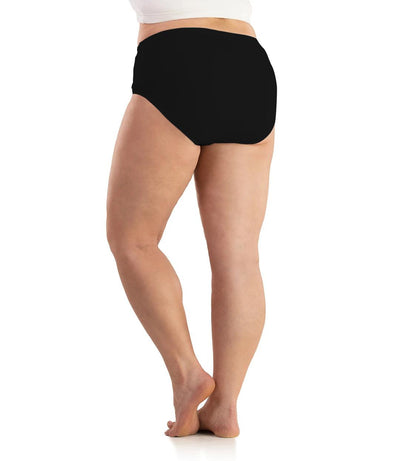 Bottom half of plus sized woman, back view, wearing JunoActive SupraKnit Briefs in black. This brief fits to the waistline with a conservative leg opening.