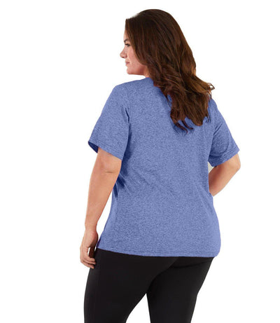 Plus size woman, facing back and looking left, wearing JunoActive plus size SoftWik V-Neck Tee in the color Heather Blue. She is wearing JunoActive Plus Size Leggings in the color black. 
