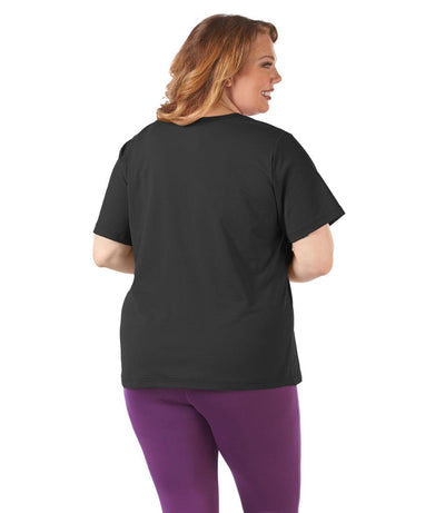 Plus size woman, facing back and looking right, wearing JunoActive plus size SoftWik V-Neck Tee in the color Black. She is wearing JunoActive Plus Size Leggings in the color Grape.