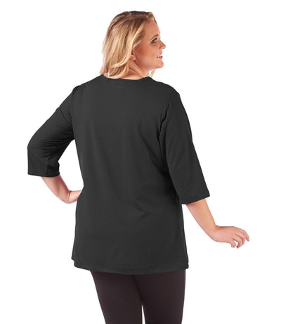 Plus size woman, facing back looking right, wearing JunoActive plus size SoftWik V-Neck Tunic with ¾ sleeves in the color Black. She is wearing JunoActive Plus Size Leggings in the color Black.