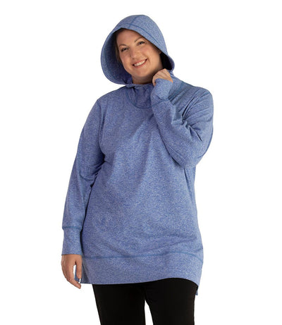 Plus size woman, facing front, wearing JunoActive plus size SoftWik Long Sleeve Hoodie in the color Heather Royal. She has the hood up on her head, covering her hair. She is wearing JunoActive Plus Size Leggings in the color Black.