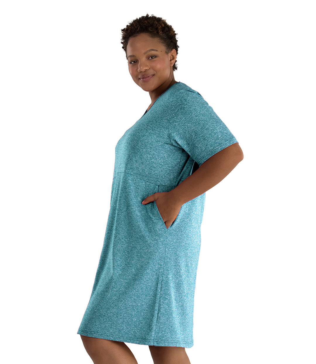 Plus size woman, facing left and looking front, wearing JunoActive plus size SoftWik Short Sleeve Dress in the color Heather Ocean. Her left hand is in the dress pocket. The dress length hits at her knee.
