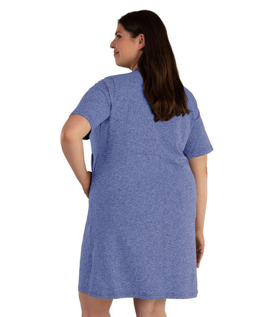Plus size woman, facing back, left arm on hip, right arm down by side. She's wearing JunoActive SoftWik short sleeve dress with pockets. Sleeves are longer and just before elbow. Hemline is above knees. The color is heather royal. 