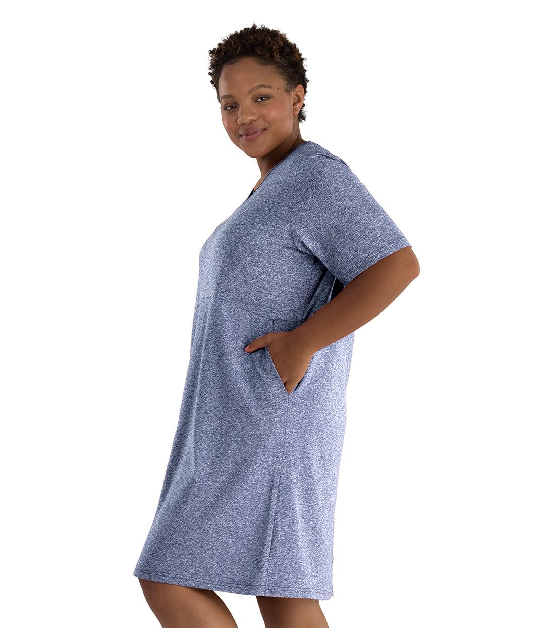 Plus size woman, facing side, left arm in pocket. She's wearing JunoActive SoftWik short sleeve dress with pockets. Sleeves are longer and just before elbow. Hemline is at knees. The color is heather navy. 