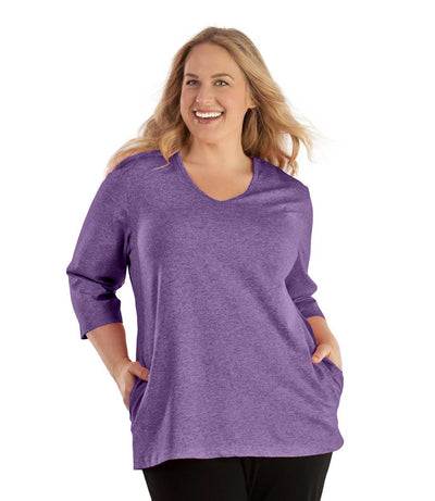 Plus size woman, facing front, wearing JunoActive plus size SoftWik V-Neck ¾ Sleeve Top with Pockets in the color Heather Amethyst. She is wearing JunoActive Plus Size Leggings in the color Black.