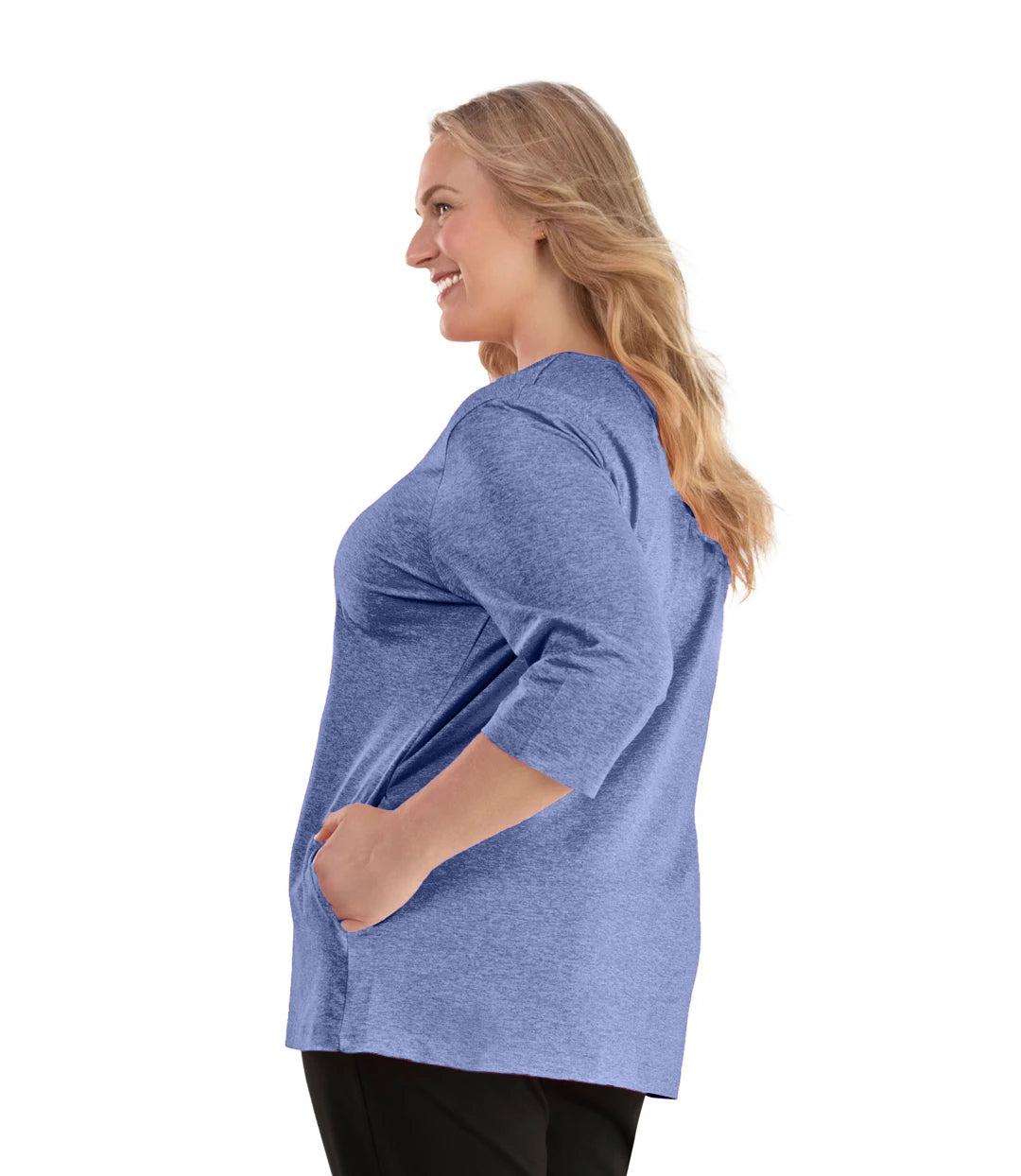 Plus size woman, facing left, wearing JunoActive plus size SoftWik V-Neck ¾ Sleeve Top with Pockets in the color Heather Royal. She is wearing JunoActive Plus Size Leggings in the color Black.