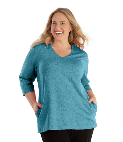 Plus size woman, facing front, wearing JunoActive plus size SoftWik V-Neck ¾ Sleeve Top with Pockets in the color Ocean Blue. She is wearing JunoActive Plus Size Leggings in the color Black.