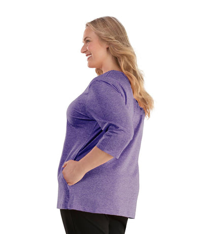 Plus size woman, facing left, wearing JunoActive plus size SoftWik V-Neck ¾ Sleeve Top with Pockets in the color Heather Violety. She is wearing JunoActive Plus Size Leggings in the color Black.
