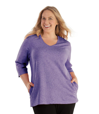 Plus size woman, facing front, wearing JunoActive plus size SoftWik V-Neck ¾ Sleeve Top with Pockets in the color Heather Violet. She is wearing JunoActive Plus Size Leggings in the color Black.