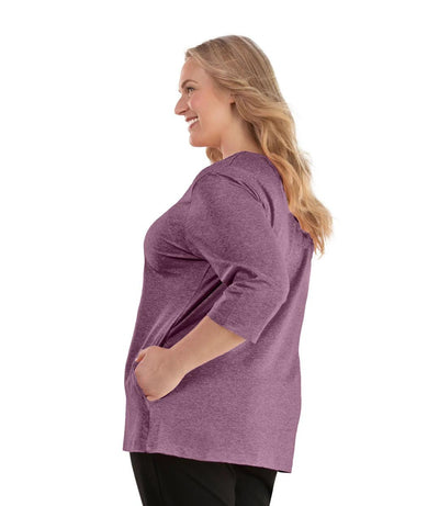 Plus size woman, facing left, wearing JunoActive plus size SoftWik V-Neck ¾ Sleeve Top with Pockets in the color Heather Merlot. She is wearing JunoActive Plus Size Leggings in the color Black.