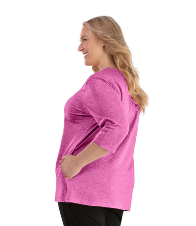 Plus size woman, facing left, wearing JunoActive plus size SoftWik V-Neck ¾ Sleeve Top with Pockets in the color Heather Fuschia. She is wearing JunoActive Plus Size Leggings in the color Black.