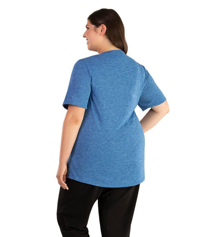 Plus size woman, facing back looking to the left, wearing JunoActive plus size QuikLite Scoop Neck Short Sleeve top in the color Heather Blue. She is wearing JunoActive Plus Size Leggings in the color black. 