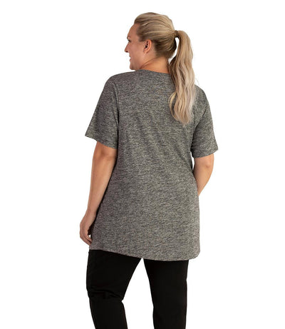 Plus size woman, facing back looking to the left, wearing JunoActive plus size QuikLite Scoop Neck Short Sleeve top in the color Heather Charcoal. She is wearing JunoActive Plus Size Leggings in the color black. 