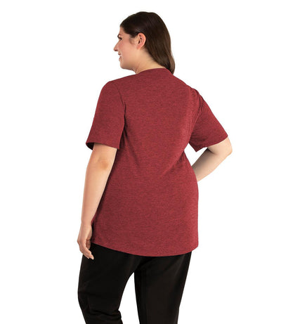 Plus size woman, facing back looking to the left, wearing JunoActive plus size QuikLite Scoop Neck Short Sleeve top in the color Heather Garnet Red. She is wearing JunoActive Plus Size Leggings in the color black. 