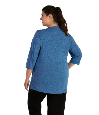 Plus size woman, facing back looking left, wearing JunoActive plus size QuikLite Scoop Neck ¾ Sleeve Top in the color Heather Blue. She is wearing JunoActive Plus Size Leggings in the color Black.