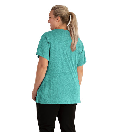 Plus size woman, facing back looking to the left, wearing JunoActive plus size QuikLite V-Neck Short Sleeve top in the color Fern Green. She is wearing JunoActive Plus Size Leggings in the color black. 