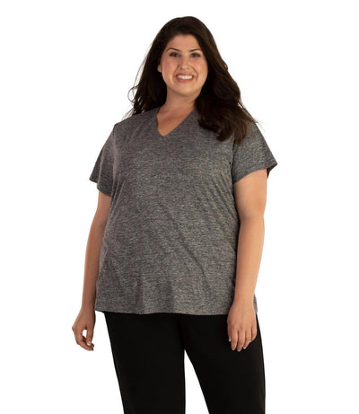 Plus size woman, facing front, wearing JunoActive plus size QuikLite V-Neck Short Sleeve top in the color Heather Charcoal. She is wearing JunoActive Plus Size Leggings in the color black. 