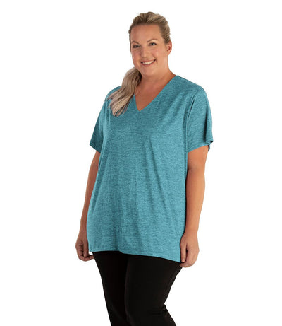Plus size woman, facing front, wearing JunoActive plus size QuikLite V-Neck Short Sleeve top in the color Heather Deep Teal. She is wearing JunoActive Plus Size Leggings in the color black. 