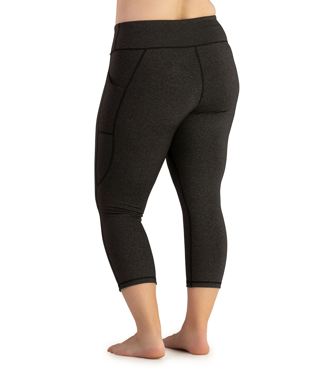 Bottom half of plus sized woman, facing back with pockets showing, wearing JunoActive JunoStretch Side Pocket Capris in heather charcoal. The hem falls a few inches above ankle and have pockets on both sides. 