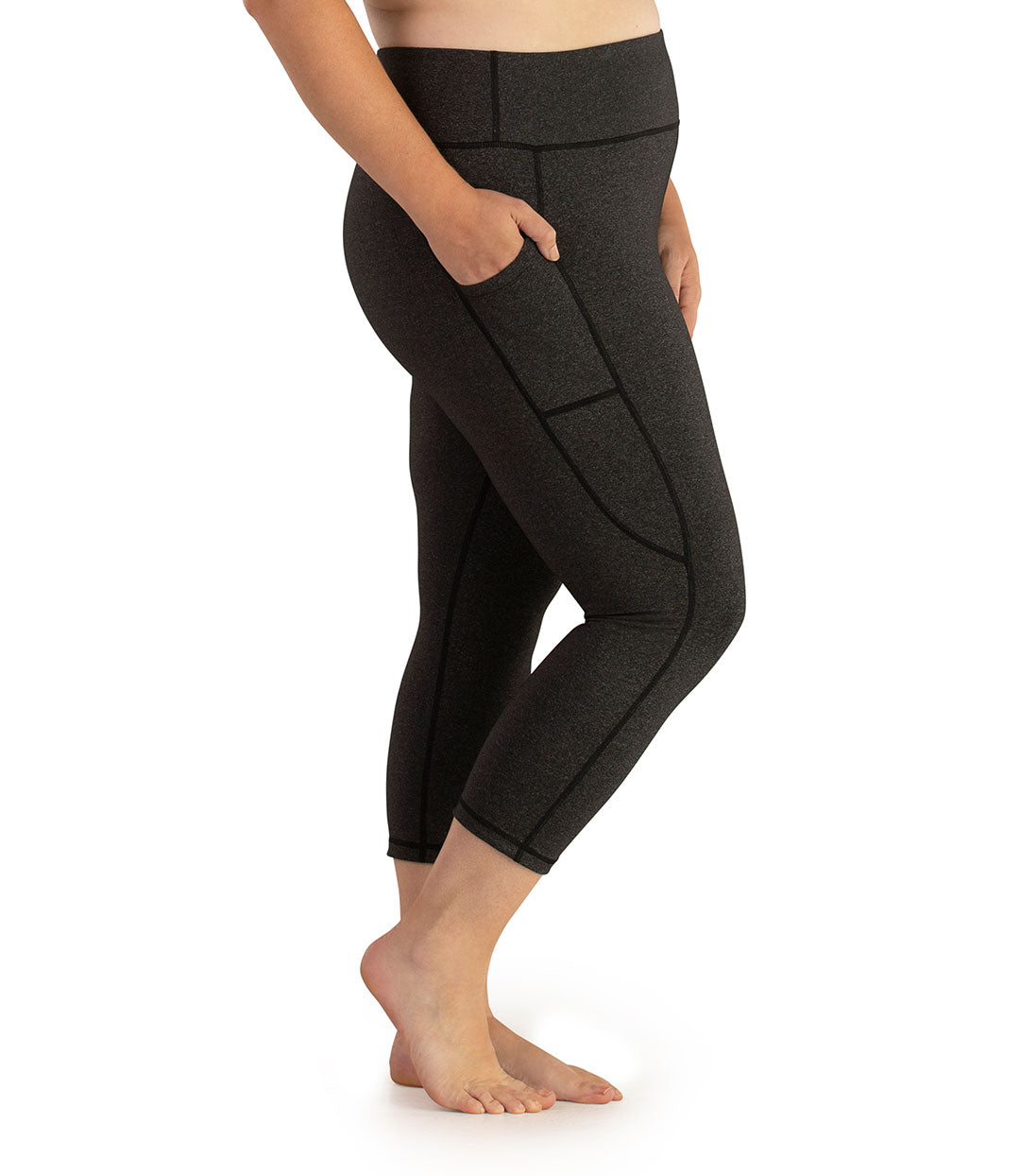 Bottom half of plus sized woman, facing side with pockets showing, wearing JunoActive JunoStretch Side Pocket Capris in heather charcoal. The hem falls a few inches above ankle and have pockets on both sides. 