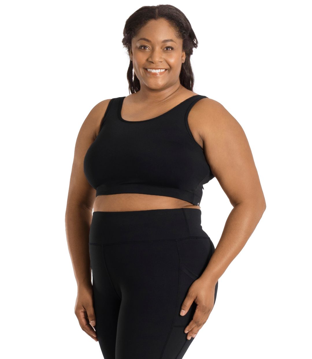 Plus size woman, facing front, wearing JunoActive plus size JunoStretch Scoop Bra in black. The woman is wearing black plus size JunoActive leggings. Her arms fall naturally to her side with her hands on her thighs. 