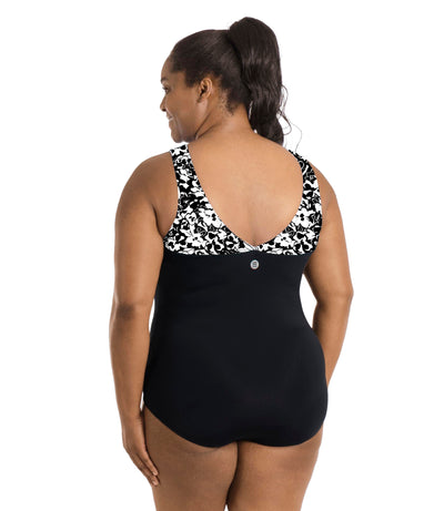 Plus size woman, facing back, wearing JunoActive plus size QuikEnergy Sweetheart Tank Suit in Hibiscus and black color blocking. The blocking on straps to a v-shape in hibiscus print. Under print is black in torso.