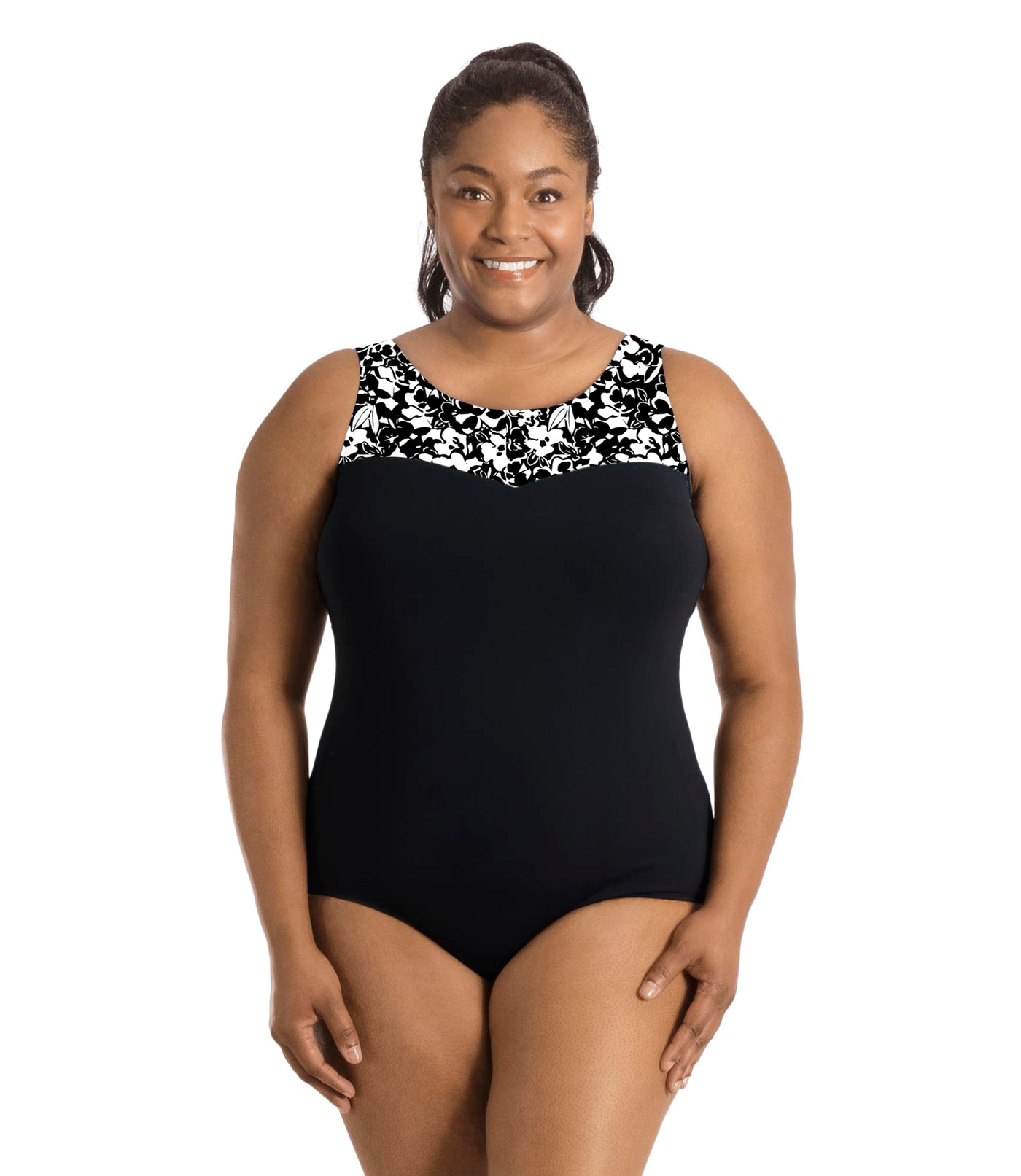 Plus size woman, facing front, wearing JunoActive plus size QuikEnergy Sweetheart Tank Suit in Hibiscus and black color blocking. The blocking at the neckline in hibiscus print. Under print is black color blocking in torso, has a scoop neckline and conservative leg opening.