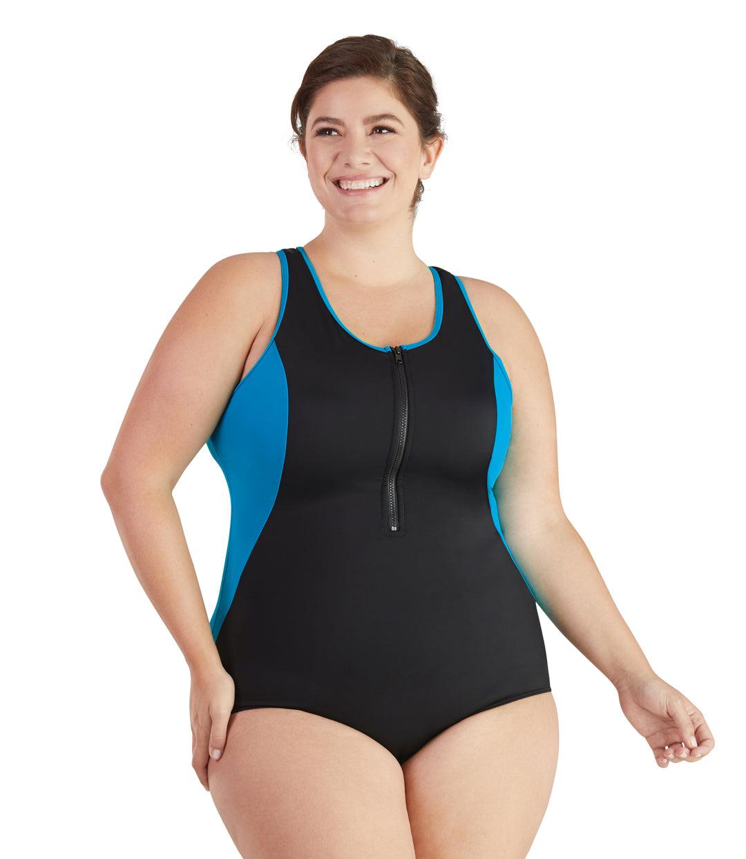 Plus size woman, facing front, wearing JunoActive plus size QuikEnergy Zip Tank Suit Turq and Black. Neck binding, armhole binding, and princess seam blocking is turquoise. The main body of the suit is solid black, has a black zipper, scoop neckline and conservative leg opening.