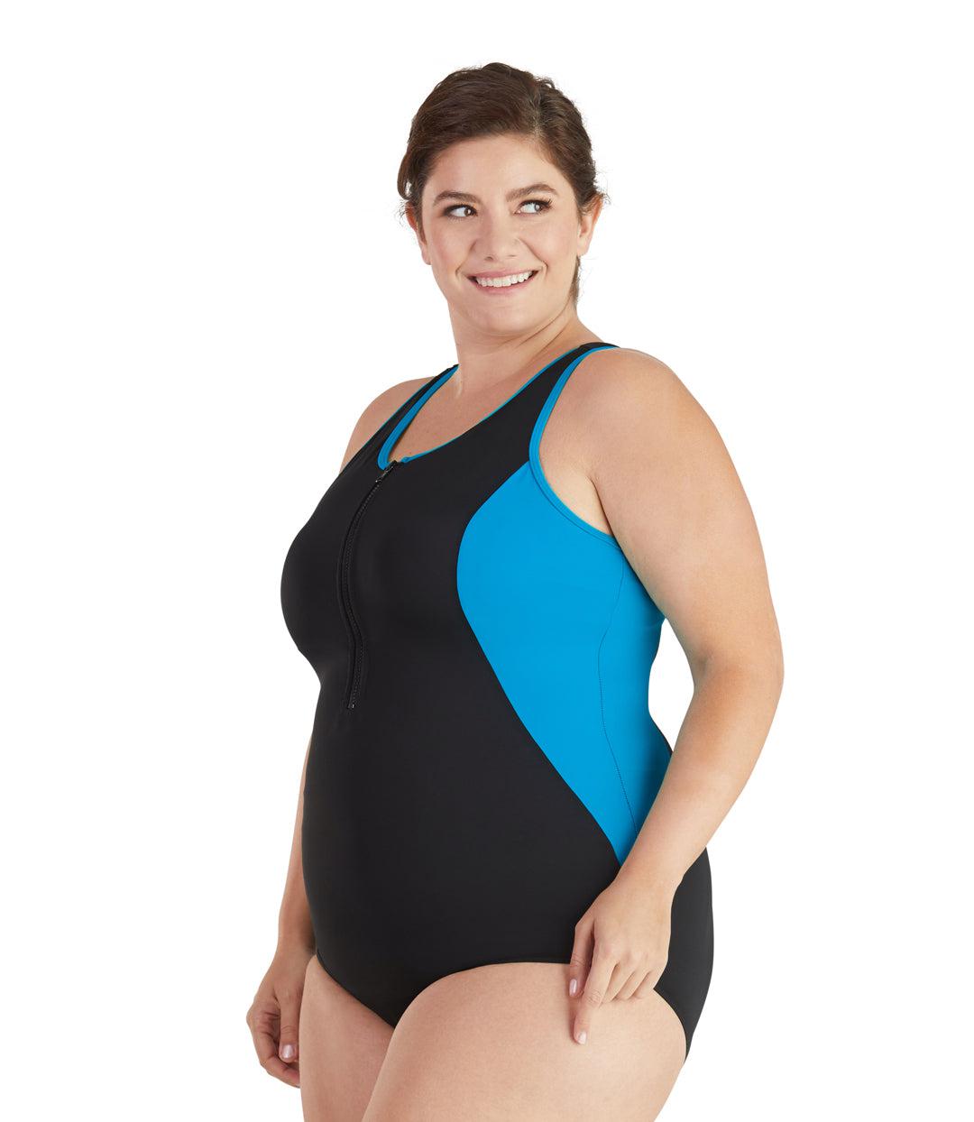 Plus size woman, facing side front looking over shoulder, wearing JunoActive plus size QuikEnergy Zip Tank Suit Turq and Black. Neck binding, armhole binding, and princess seam blocking is turquoise. The main body of the suit is solid black, has a black zipper, scoop neckline and conservative leg opening.