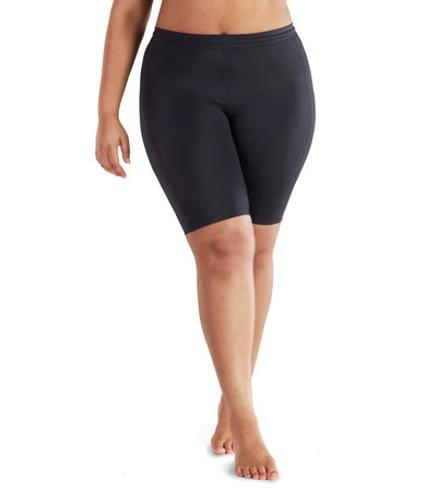 Bottom half of plus size woman facing front wearing JunoActive QuikEnergy Fitted Swim Short. The short is black and is tight to the body. The hem is just above the knee.