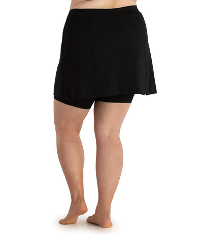 Plus size woman, back view, wearing  QuikEnergy Swim Skirt with Short Black. The overlay of skirt is black with solid black shorts underneath. 
