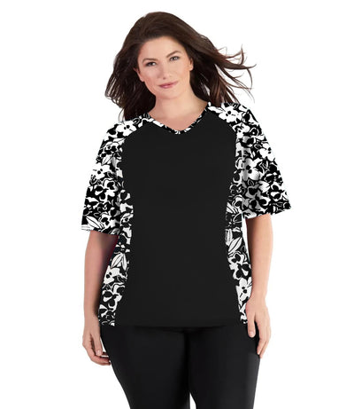 Plus size woman, facing front wearing JunoActive QuikEnergy Lite Swim and Beach short Sleeve Top Hibiscus Black. Solid Black on the center torso and Hibiscus print on the sleeves and side panels. The short sleeves end at the elbow.