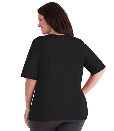 Plus size woman, back view, wearing QuikEnergy Short Sleeve Swim and Sun Top South Pacific Black. Solid black back and sleeves. Long cover short sleeves meeting at the elbow. 