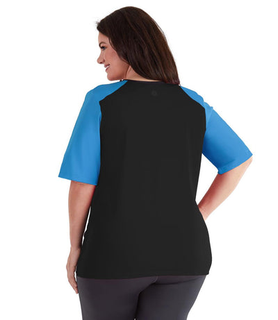 Plus size woman, back view, wearing QuikEnergy Short Sleeve Swim and Sun Top Black and Turq. Solid black back and turquoise colorblocking on the sleeves. Long cover short sleeves meeting at the elbow. 