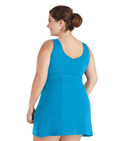Plus size woman, back view, wearing JunoActive plus size QuikEnergy Swim Dress Turquoise. The dress is solid Turquoise, has a scoop neckline, slight a-line shape and ends mid-thigh.