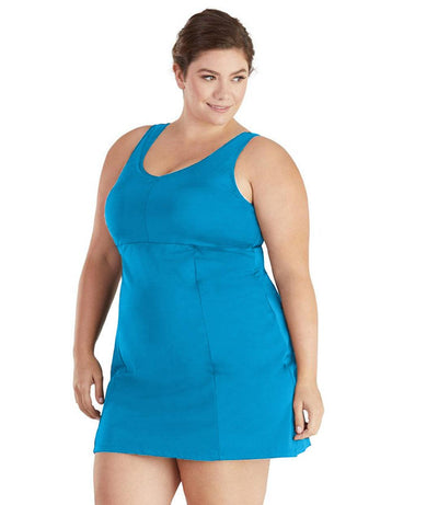 Plus size woman, facing front, wearing JunoActive plus size QuikEnergy Swim Dress Turquoise. The dress is solid Turquoise, has a scoop neckline, slight a-line shape and ends mid-thigh.