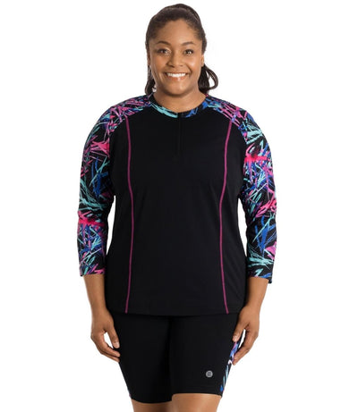 Plus size woman, front facing view, wearing AquaSport Long Sleeve Rash Guard Sunset Palm Print Black. Pink, blue and teal abstract line print colorblock accent on shoulders and pink princess seams down the front. 7/8 sleeve length.  