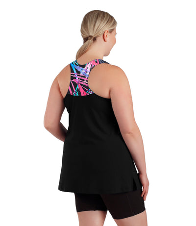 Plus size woman, facing back view, wearing AquaSport Hanalei Tankini Top Sunset Palm Print Black. The back of the tankini is razor back with the top portion covered in pink, blue and teal abstract line print. The bottom of the tankini is solid black falling right below the bottom. 