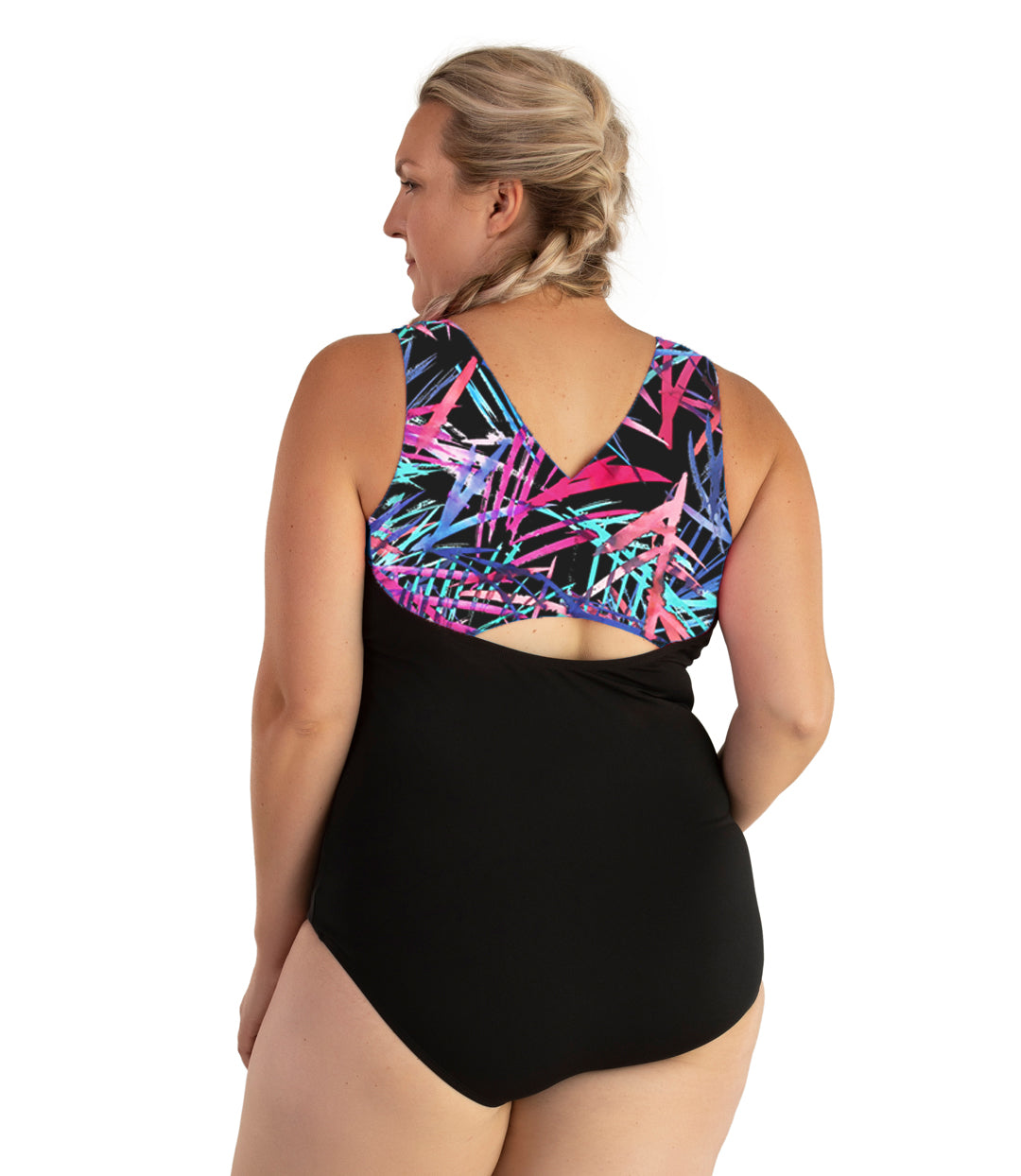 Plus size woman, back view, wearing JunoActive plus size AquaSport Crossback Tanksuit Sunset Palm Print Black. The crossback shoulder detail of the tanksuit has multi colored pink blue and black Palm print. The main body of the suit is solid black, keyhole opening at the mid-back.